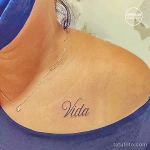 Фото тату: надпись 'Vida' (Жизнь) выполненная изящным шрифтом на груди женщины.