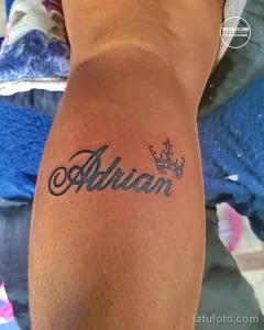 Фото тату на руке с именем 'Adrian', написанным красивым каллиграфическим шрифтом, и небольшой звездой рядом. Рисунок выполнен в черном цвете.