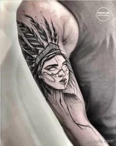 Фото тату портрета индейки на плече в стиле blackwork. Детализированное изображение лица, перьев и головного убора.