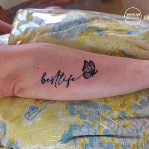 Фото тату: небольшая татуировка с надписью "best life" и изображением бабочки на руке. Черные чернила и минималистичный дизайн.
