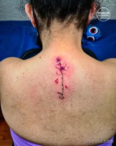 Фото тату: небольшая татуировка с изображением цветка сакуры и надписью 'Chuma' на шее. Простой и элегантный эскиз татуировки.