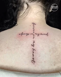 Фото тату: изящная надпись «forever in my mind, always in my heart» вертикально на затылке девушки, выполненная тонкими линиями.