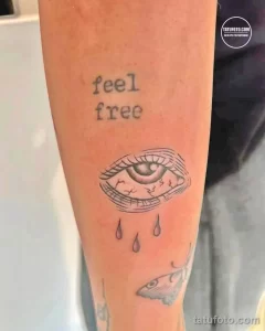 Фото тату глаза с текущими слезами и надписью 'feel free' на руке. Эмоциональный рисунок татуировки в стиле графика.