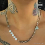 Фотография татуировки, имитирующей украшение на теле: цепочка с кулоном и жемчугом. Татуировка выглядит как аксессуар.