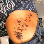Фото татуировки с изображением одуванчика, из которого разлетаются птицы. Тату выполнено в минималистичном стиле с тонкими линиями.