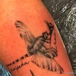 Фото татуировки с изображением голубя, держащего цветок, и надписями имен 'Lana' и 'Larisa'. Черно-белый рисунок.