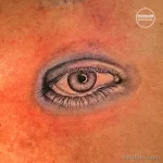 Фото тату реалистичного глаза на плече. Детализированная прорисовка радужки, зрачка и ресниц. Черно-серые тона, реалистичный стиль.