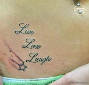 Фото тату надписи 'Live, Love, Laugh' на боку. Черно-красная татуировка с небольшим изображением звезды. Изящный шрифт и минималистичный дизайн.