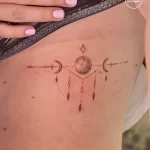 Фото тату луны и звезд на боку, выполненное в минималистичном стиле. Детализированный рисунок татуировки с использованием тонких линий и точек.