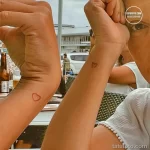 Фото минималистичных татуировок в виде сердца на запястьях двух людей. Простые линии татуировки символизируют любовь и близость.