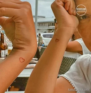 Фото минималистичных татуировок в виде сердца на запястьях двух людей. Простые линии татуировки символизируют любовь и близость.