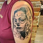 Фото тату: татуировка в стиле "сахарная черепушка" (sugar skull) с цветами, выполненная в черно-серых тонах на руке.