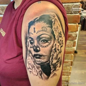 Фото тату: татуировка в стиле "сахарная черепушка" (sugar skull) с цветами, выполненная в черно-серых тонах на руке.