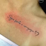 Фото тату: небольшая надпись на португальском языке "Seja forte e corajosa" (Будь сильной и смелой) с маленьким сердечком. Простой и вдохновляющий эскиз тату.