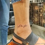 Фото тату надписи 'A la folie' на лодыжке. Изящный шрифт, черный цвет, минималистичный дизайн, подходит для любителей французского языка.