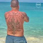 Фото тату на спине мужчины с надписью 'La Familia' и изображением ворона, выполненное в стиле традиционной татуировки.