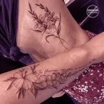 Красивая черно-белая татуировка с изображением различных цветов и французской надписью на руке.