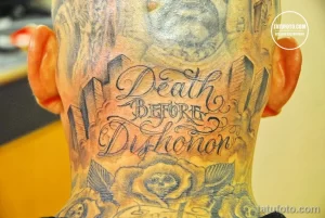 Фото тату: надпись "Death Before Dishonor" и изображение черепа на затылке мужчины. Татуировка выполнена в серо-черных тонах.