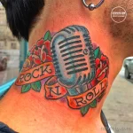 Фото тату на шее с изображением винтажного микрофона, обвитого красными розами и надписью 'Rock N Roll'. Яркий и стильный рисунок татуировки.