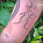 Черно-белое фото минималистичной татуировки лица, выполненной в технике line art на руке. Изображение дополнено надписью 'ART'.
