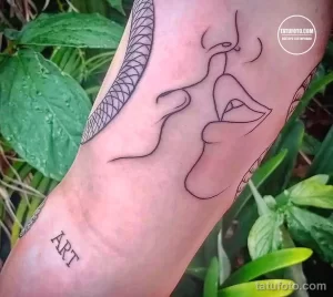 Черно-белое фото минималистичной татуировки лица, выполненной в технике line art на руке. Изображение дополнено надписью 'ART'.