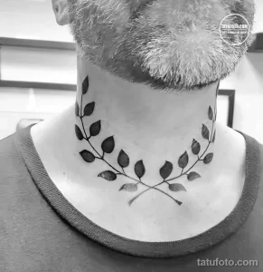 Фотография татуировки в виде венка из листьев на шее мужчины. Татуировка выполнена в черно-белых тонах и имеет минималистичный дизайн.
