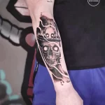 Фото тату: реалистичный череп в мотоциклетном шлеме на предплечье. Черно-серый рисунок с высокой детализацией.