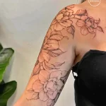 Фото тату: реалистичные цветы пиона в технике line work на плече и предплечье. Черно-белый рисунок татуировки с детальной проработкой лепестков и листьев.