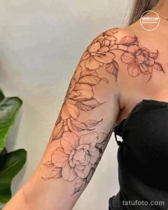 Фото тату: реалистичные цветы пиона в технике line work на плече и предплечье. Черно-белый рисунок татуировки с детальной проработкой лепестков и листьев.