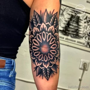 Фото тату в стиле blackwork на руке: крупный подсолнух, выполненный полностью черным цветом, с детализированными лепестками и центром. Геометрический узор.
