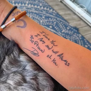 Фото тату: надпись "I Love You I Am and will Always Be Proud of You" на руке. Черная татуировка выполнена от руки, создавая эффект искренности и личного послания.