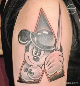 Фото тату, изображающее Микки Мауса в необычном исполнении с добавлением мрачных элементов, таких как глаз и трещины.