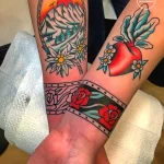 Фото парных тату на предплечьях двух людей. На одной руке изображены горы и цветы эдельвейса, на другой - яблоко и розы в традиционном стиле.