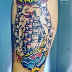 Фото татуировки в традиционном морском стиле на руке мужчины. Изображение корабля, окруженного ласточками и розами.