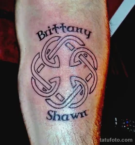 Фото татуировки кельтского узла с надписями имен 'Brittany' и 'Shawn' на предплечье. Тату выполнено в черном цвете, с четкими линиями и каллиграфическим шрифтом.