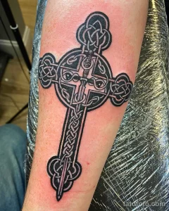 Фото тату кельтского креста с мечом, проходящим через него. Черно-белый рисунок татуировки выполнен в детальной графике.