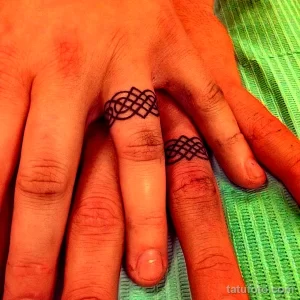 Фото тату: два пальца с маленькими черными кельтскими узлами, обвивающими их как кольца. Минималистичный и стильный рисунок татуировки.