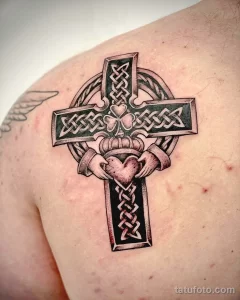 Фото татуировки кельтского креста с сердцем и клевером на плече. Черно-белый рисунок с детальной проработкой узоров и символов.