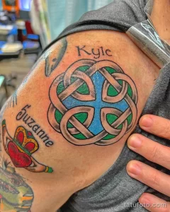 Фото тату кельтского узла с именами 'Kyle' и 'Suzanne' на плече, выполненного в ярких цветах: синем, зеленом и черном.