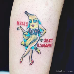 Фото тату банана в красном бикини с надписями 'Hello' и 'Sexy Banana!'. Яркий, красочный рисунок татуировки в стиле пин-ап.