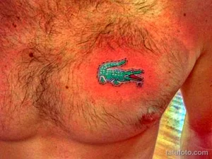 Фото тату логотипа Lacoste (крокодил) в зеленых и черных тонах. Рисунок выполнен в минималистичном стиле и расположен на груди.