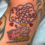 Фото тату паровоза с надписью "I CHOO-CHOO-CHOOSE YOU" и сердечками. Рисунок выполнен в ярких цветах в стиле old school.