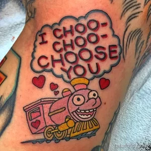 Фото тату паровоза с надписью "I CHOO-CHOO-CHOOSE YOU" и сердечками. Рисунок выполнен в ярких цветах в стиле old school.