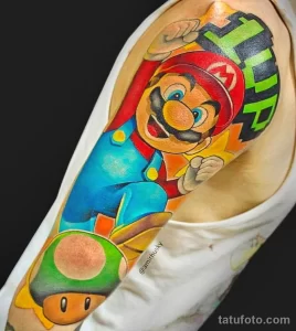 Фото тату: яркий рисунок Марио из игры Super Mario, в прыжке на фоне кирпичной стены, выполненный в стиле поп-арт. Расположение - предплечье.