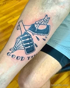 Фото тату на ноге с изображением скелета, держащего бутылку, и надписью "Good Times". Стильный и символичный рисунок.