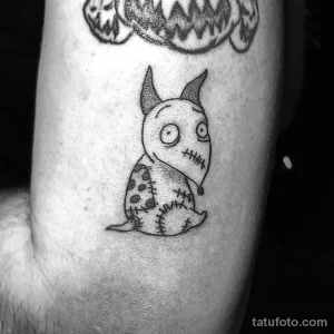 Маленькая черно-белая татуировка в виде забавного монстра с швами и рожками. Милый и оригинальный дизайн для любителей необычных тату.