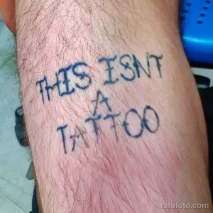 Фото тату с надписью 'THIS ISN'T A TATTOO' на руке. Ироничный рисунок татуировки, пример самоиронии и юмора.