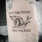Фото тату на руке: улитка с крыльями и надписью "Buy the ticket take the ride". Мотивирующая и оригинальная татуировка.