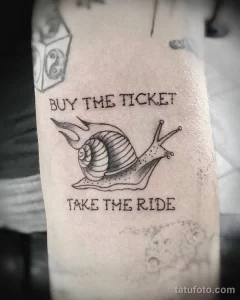 Фото тату на руке: улитка с крыльями и надписью "Buy the ticket take the ride". Мотивирующая и оригинальная татуировка.
