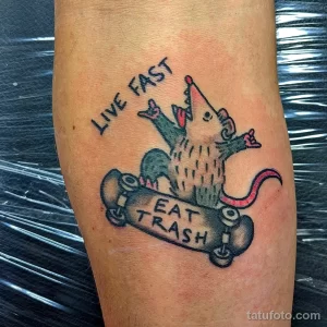 Фото тату крысы, катающейся на скейтборде, с надписью 'Live Fast Eat Trash'. Стиль олдскул, яркие цвета, предплечье.
